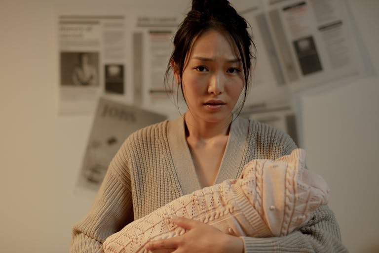 A concerned mother embraces her newborn indoors, surrounded by newspaper articles. Postpartum Depression vs. Baby Blues – Know the Difference