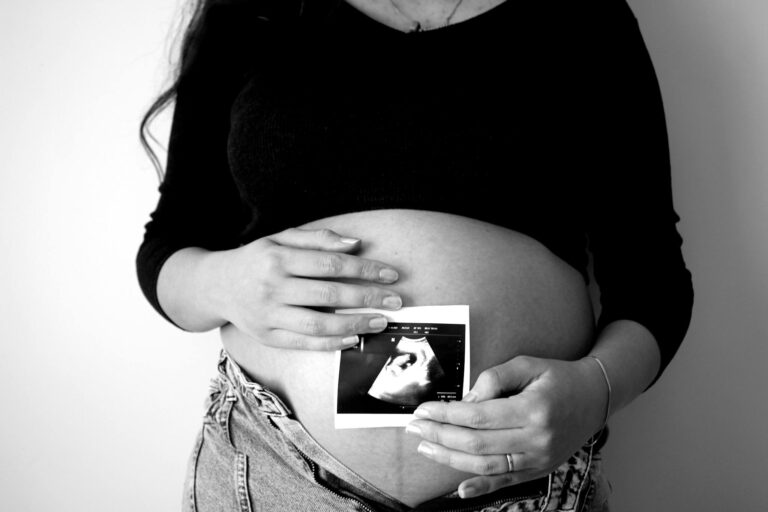 A pregnant woman holds an ultrasound photo against her belly, symbolizing expecting motherhood. mental health