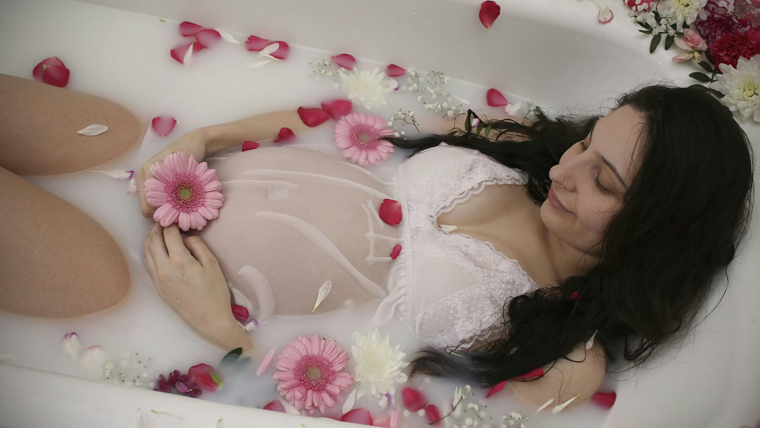 A serene pregnant woman relaxes in a milk bath adorned with pink flowers, symbolizing maternity. 15 Self-Care Ideas for the Exhausted Pregnant Woman