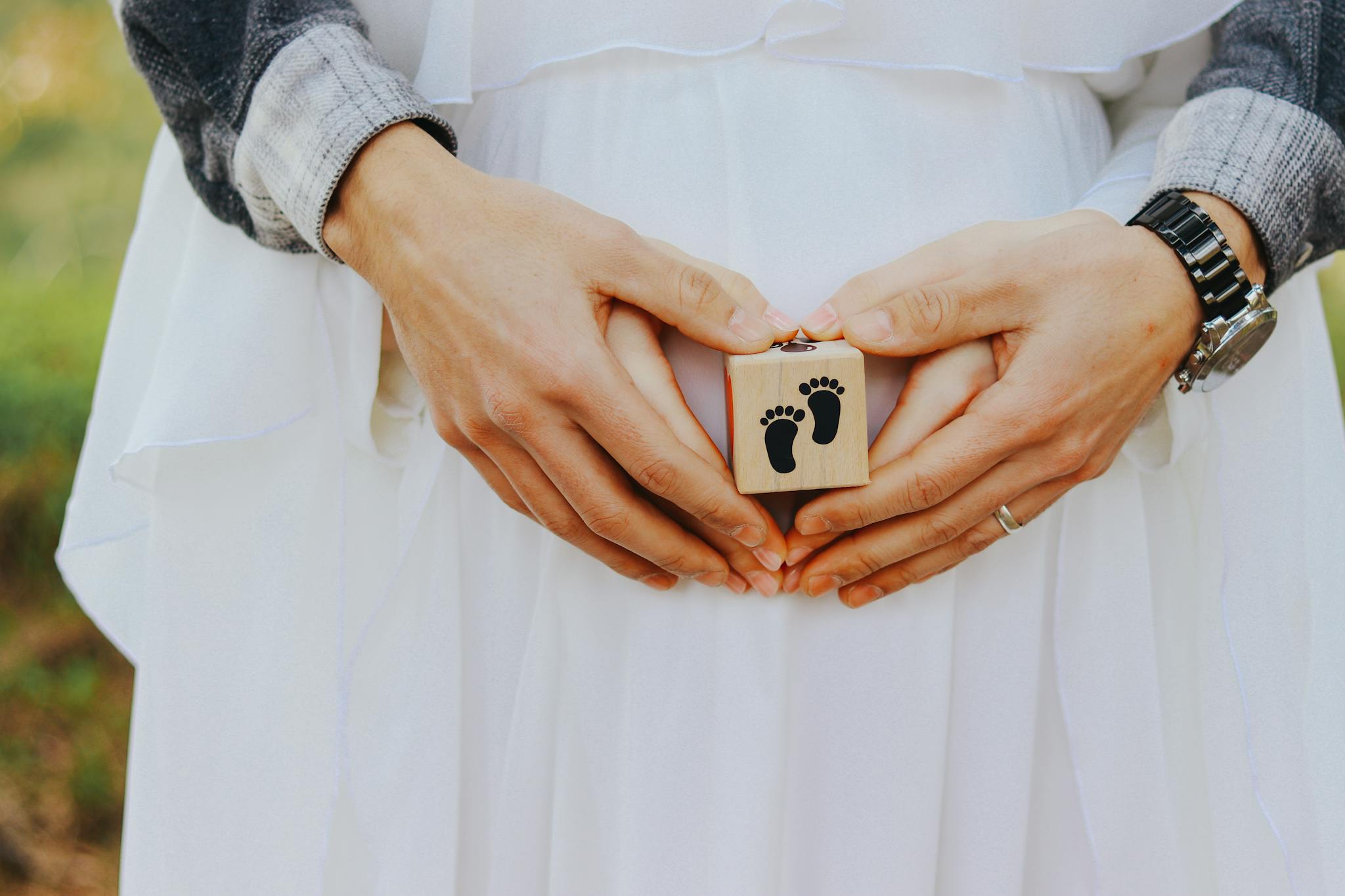 Close-up of a couple's hands on pregnant belly holding a small wooden block with baby footprints.