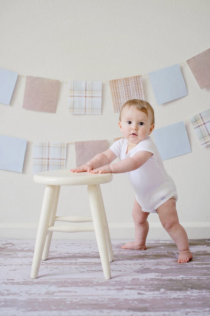 Cute baby standing by a stool indoors with a playful background. Baby Essentials (Pre-Birth Prep)