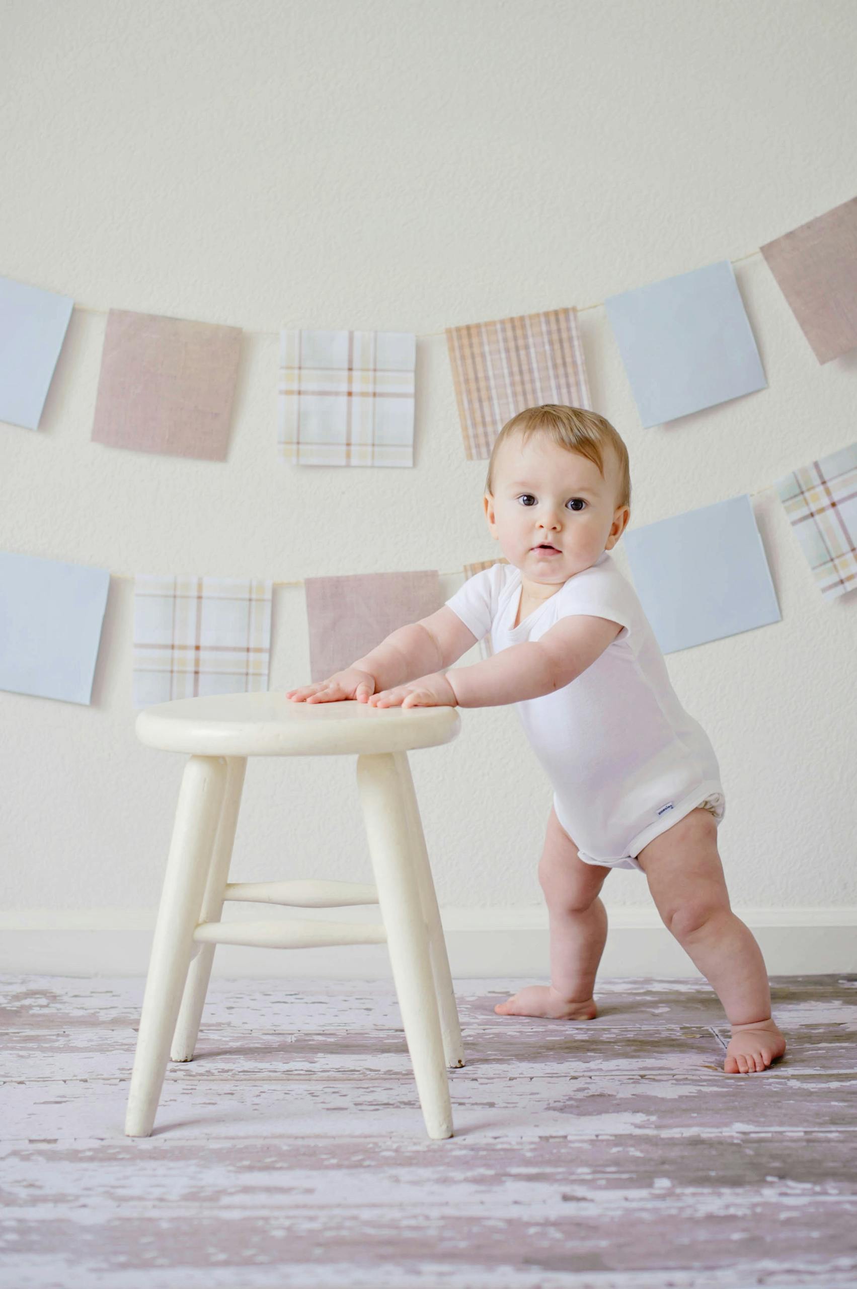 Cute baby standing by a stool indoors with a playful background. Baby Essentials (Pre-Birth Prep)