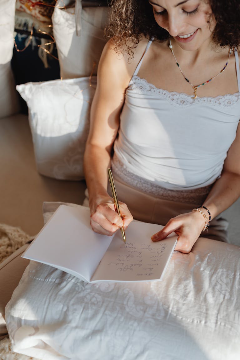 A brunette woman writes and smiles while sitting comfortably indoors with a notebook. Journaling Ideas for Mom-To-Be: A Beautiful Way to Capture Your Pregnancy Journey
