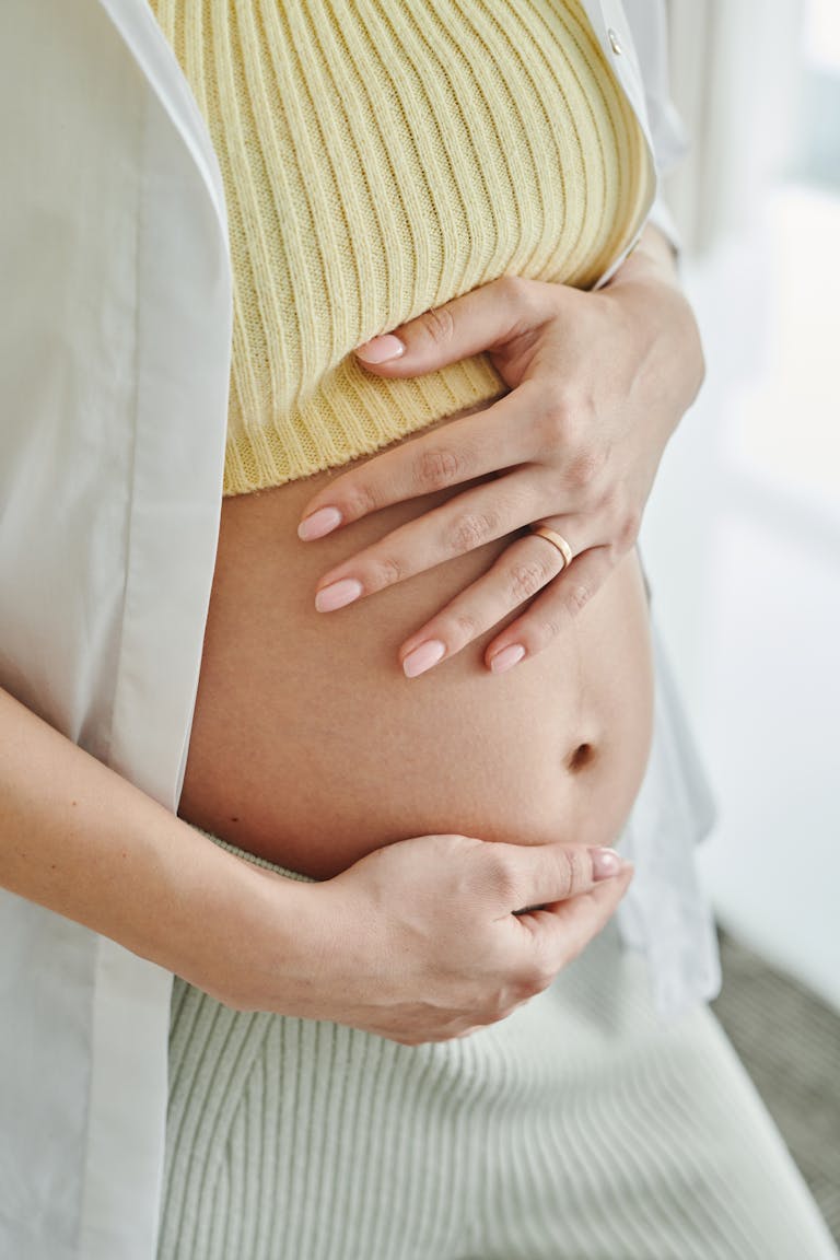 A close-up shot of a pregnant woman's hands gently resting on her belly, symbolizing motherhood. do