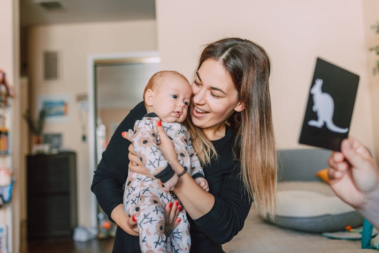 A joyful mother holds her baby, engaging them with a kangaroo flashcard indoors. FAQ Preparing Mentally for Motherhood Your Questions About the Emotional Transition Answered