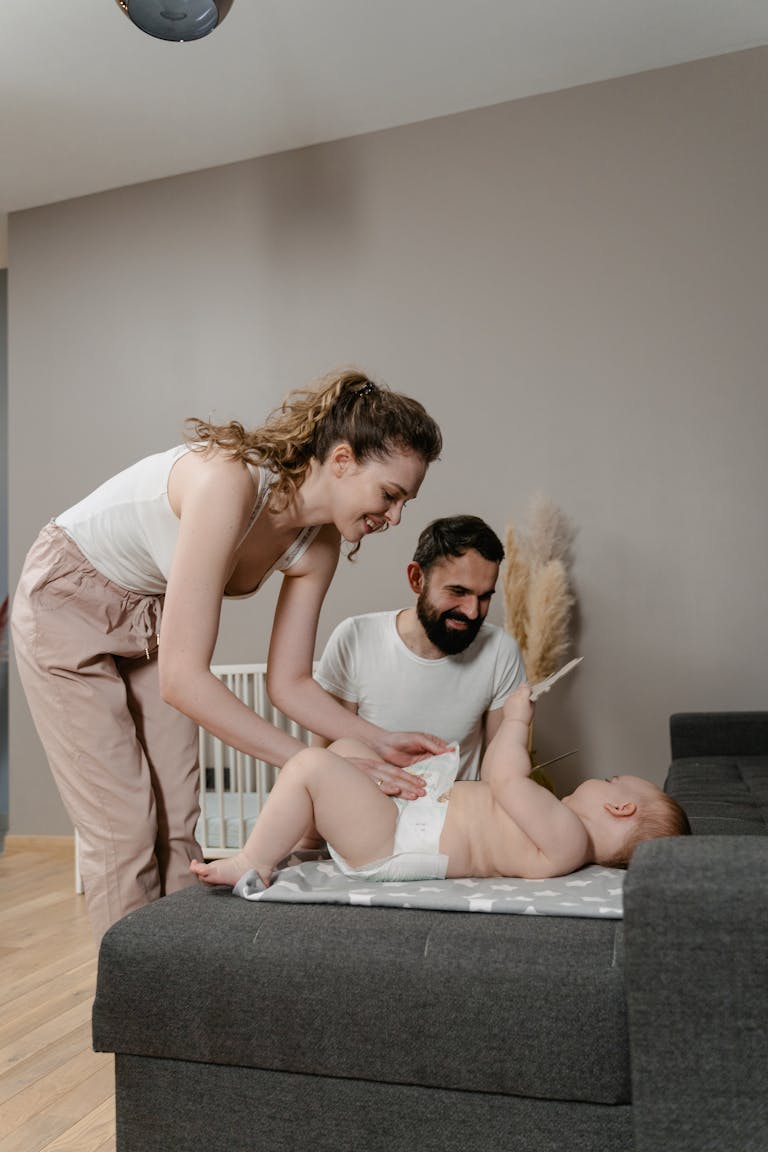 A loving couple changes their baby's diaper on a couch, exuding warmth and care in a cozy home environment. diapering