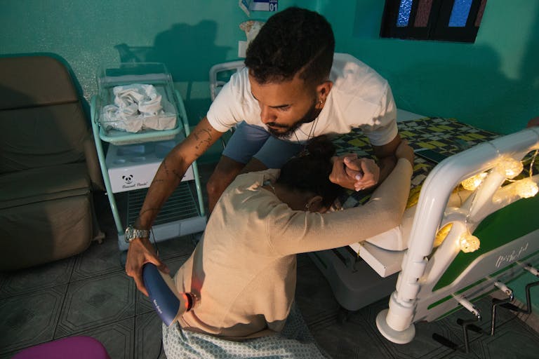 A man supports a woman in labor at a hospital bedside, holding her hand and using a device for comfort. Understanding the Latent Phase of Labor: What No One Tells You