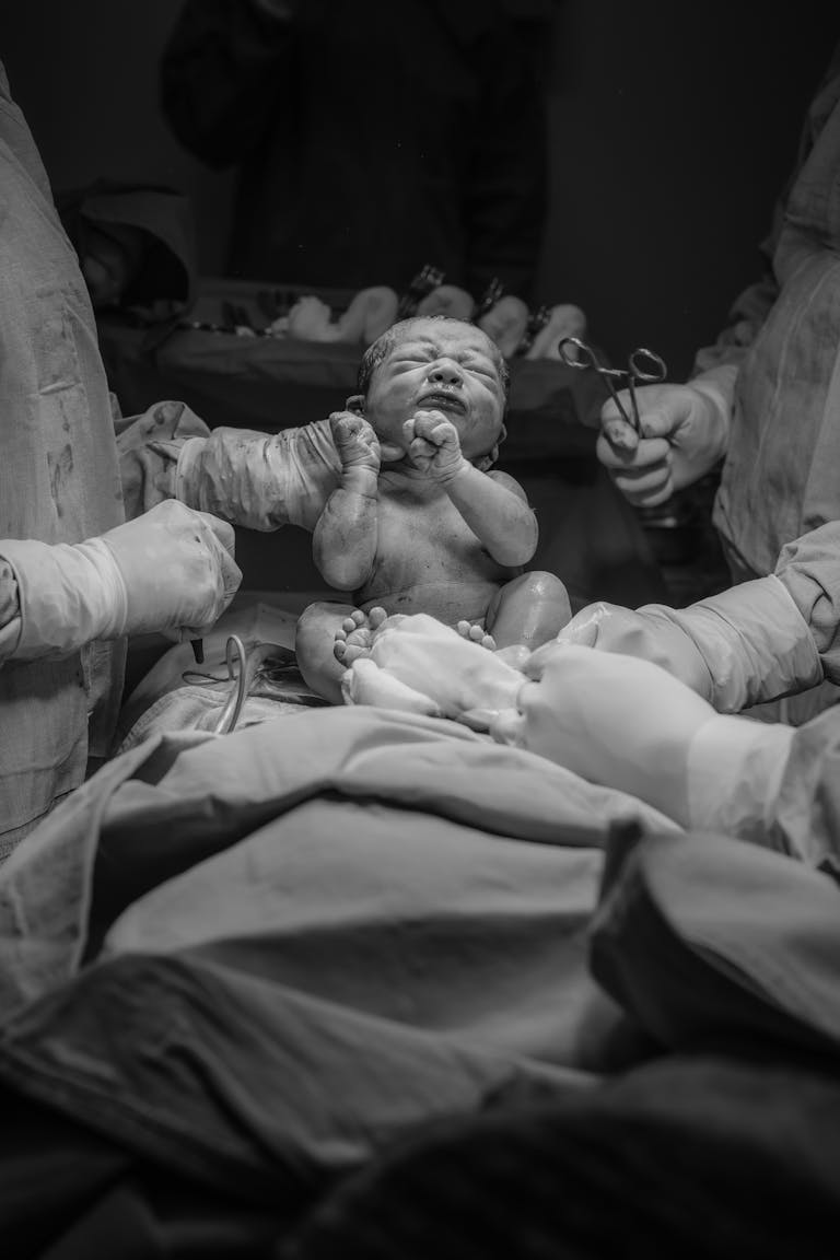 A touching black and white image of a newborn baby in a hospital setting during childbirth.