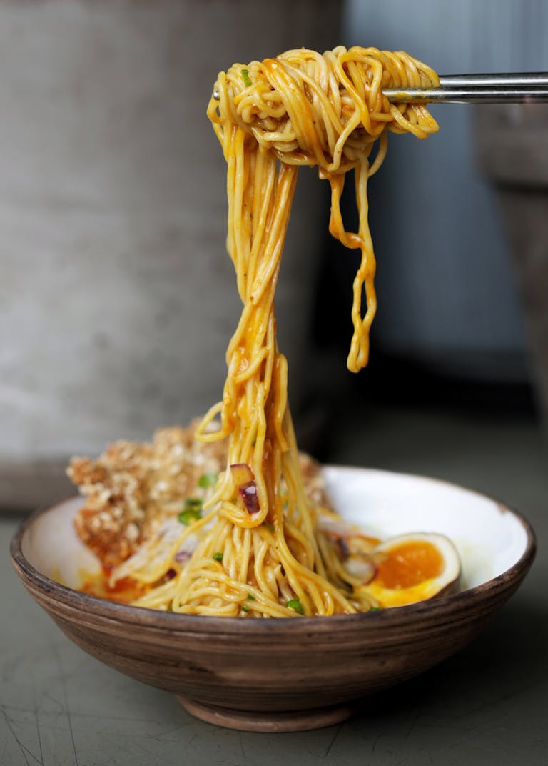 Close-up of savory ramen noodles in a bowl with egg and greens.