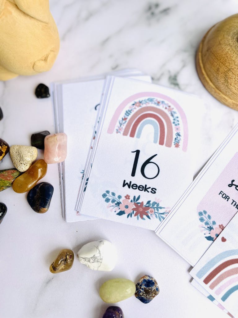 Colorful milestone card displaying '16 Weeks' with a rainbow design surrounded by decorative stones.