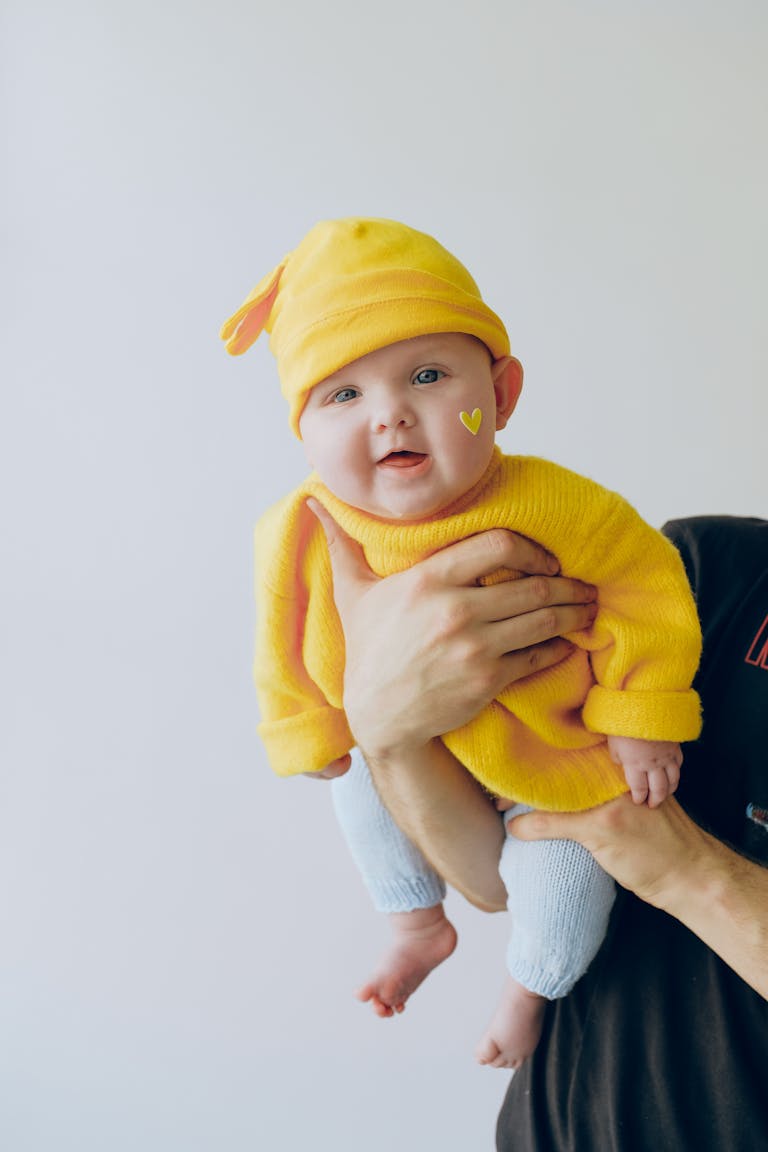Cute baby in a yellow outfit being held indoors against a light background. 🍼 Newborn Essentials List: Everything You Need for Your Baby’s First Months