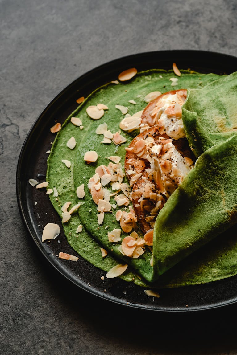 Delicious green spinach crepes served with cream cheese and almond flakes on a black plate. Iron-Rich Foods in Pregnancy: Boosting Energy and Baby’s Development