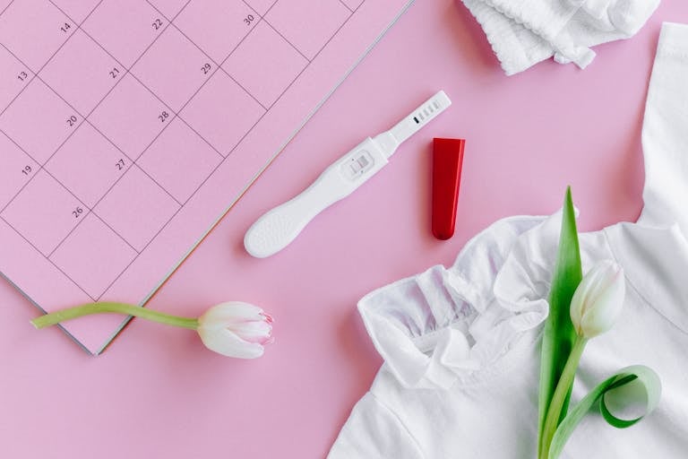 Flat lay of a pregnancy test with tulips on a pink calendar surface, symbolizing fertility and new life.