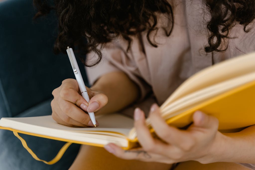 Person writing in a yellow notebook indoors, focusing on ideas. Journaling Ideas for Mom-To-Be: A Beautiful Way to Capture Your Pregnancy Journey