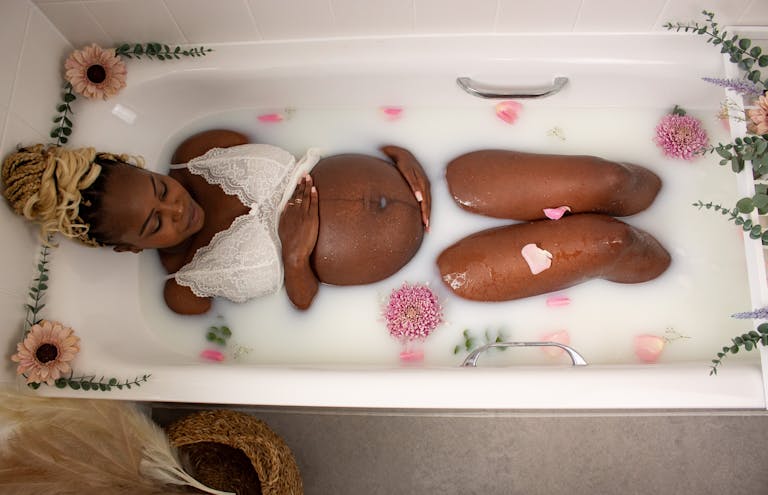 Pregnant woman enjoying a relaxing floral milk bath for a serene maternity experience. 🌸 Mom-To-Be Pampering Guide: Because You Deserve It, Mama!