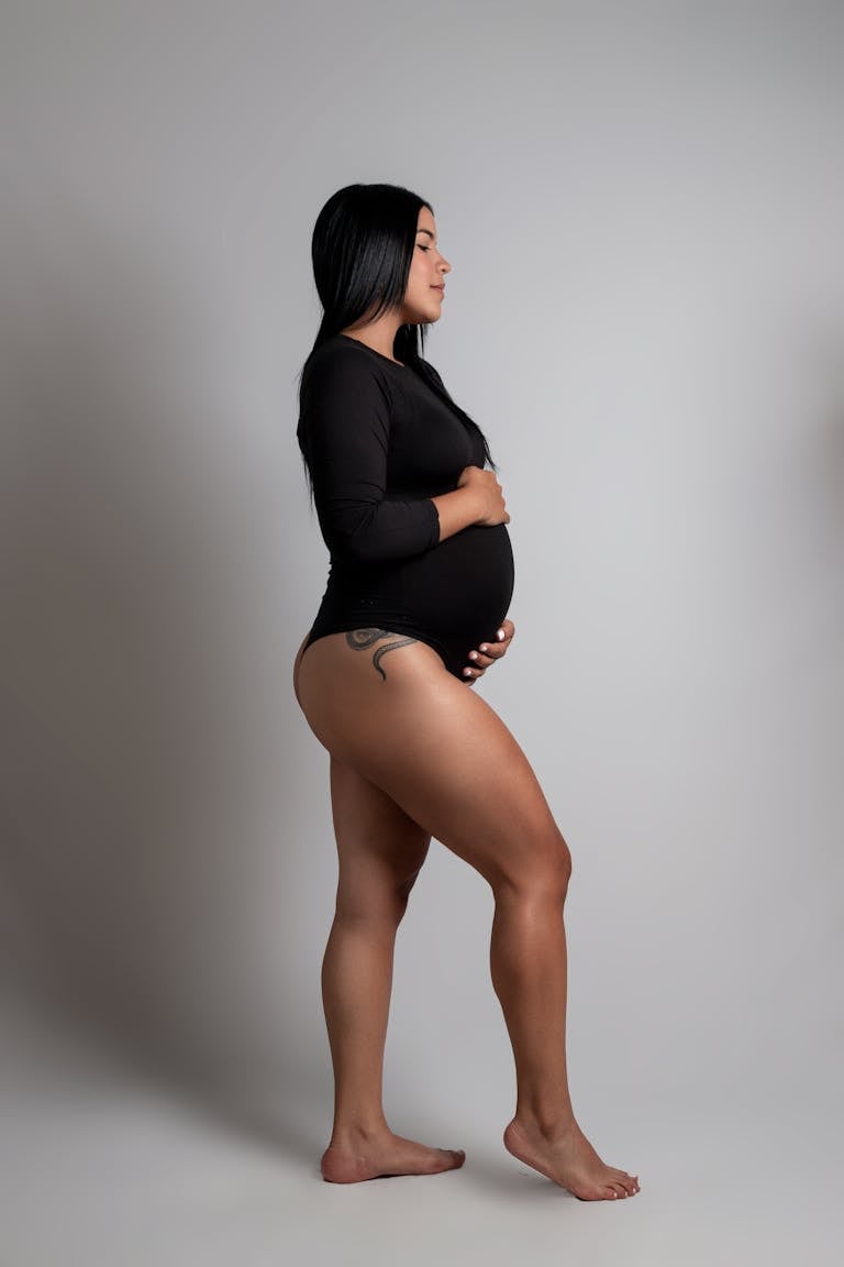 Side profile of a pregnant woman posing barefoot in black bodysuit against a white background. Week 32 of Pregnancy: The Final Countdown Begins!