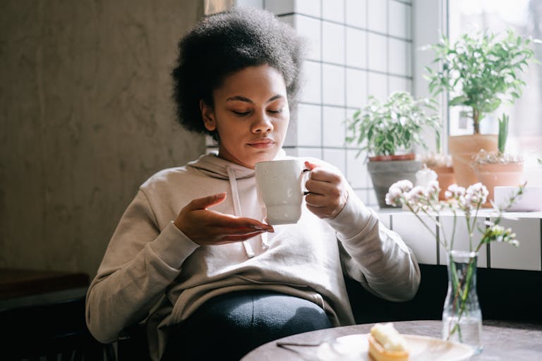 Woman enjoying a peaceful moment sipping tea by a window with indoor plants. The Morning Sickness Survival Guide You Wish You Had Sooner
